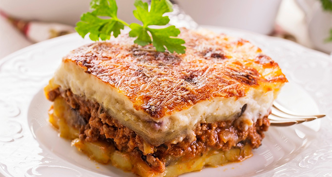 delicious layer of moussaka with ground meat and potatoes topped with creamy sauce garnished with parsley perfect for eight servings